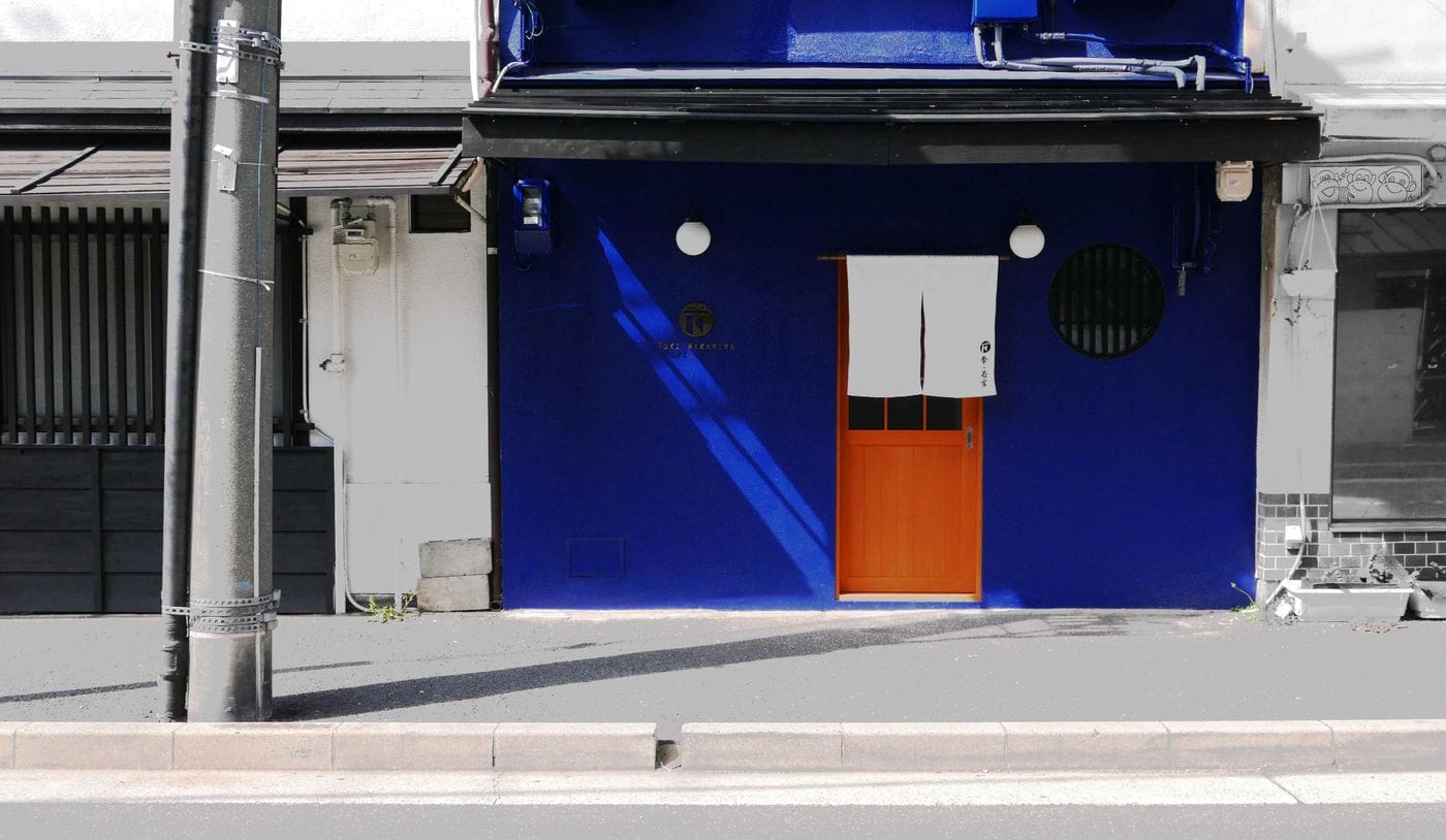 Vibrant blue facade in Kyoto with a traditional noren curtain and wooden door on a sunny day.