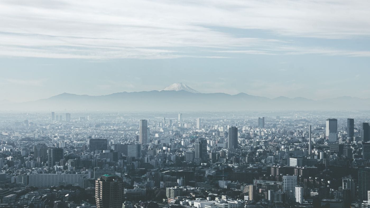 Panoramic view of Tokyo cityscape with Mount Fuji looming in the background, under cloudy skies.