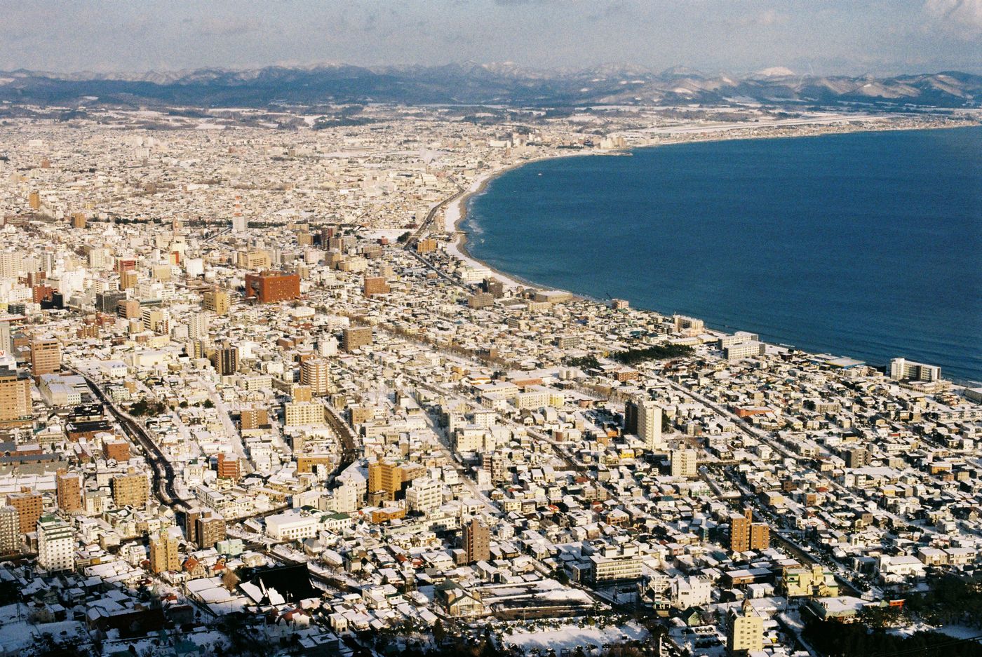 Stunning aerial view of a snow-covered coastal city meeting the blue sea during winter.
