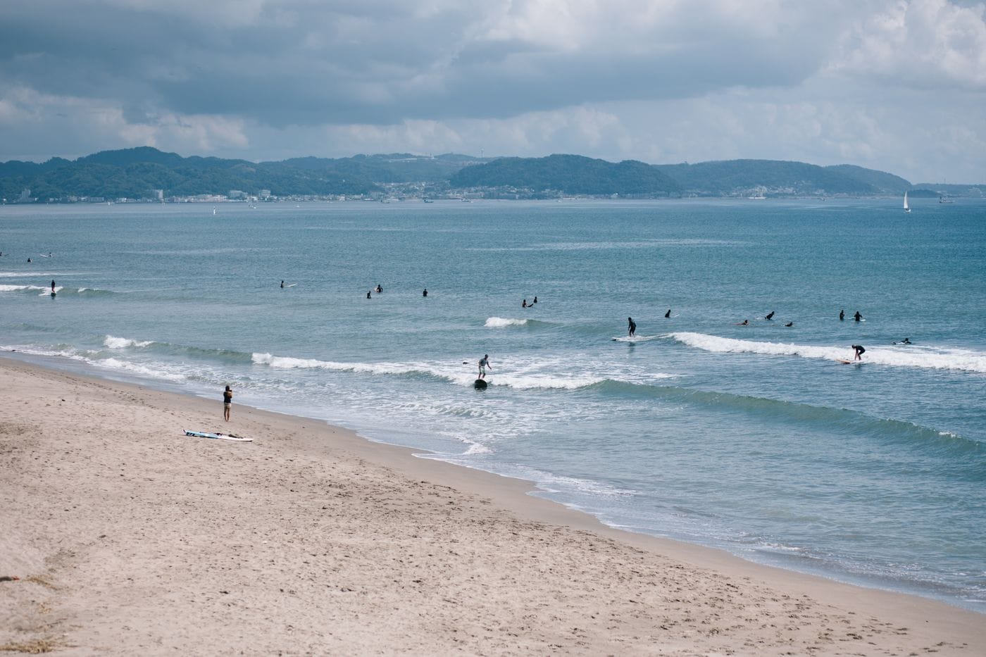 Group of surfers enjoying the waves on a peaceful sandy beach under cloudy skies.