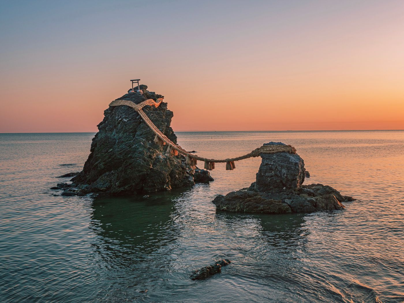 Photograph of the Meoto Iwa sacred rocks at sunrise, a spiritual site in Japan's ocean.