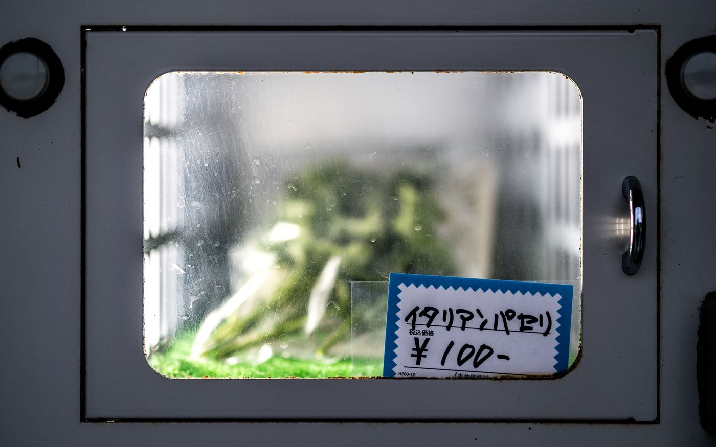 A vending machine window displaying Italian parsley priced at 100 yen in Japan.