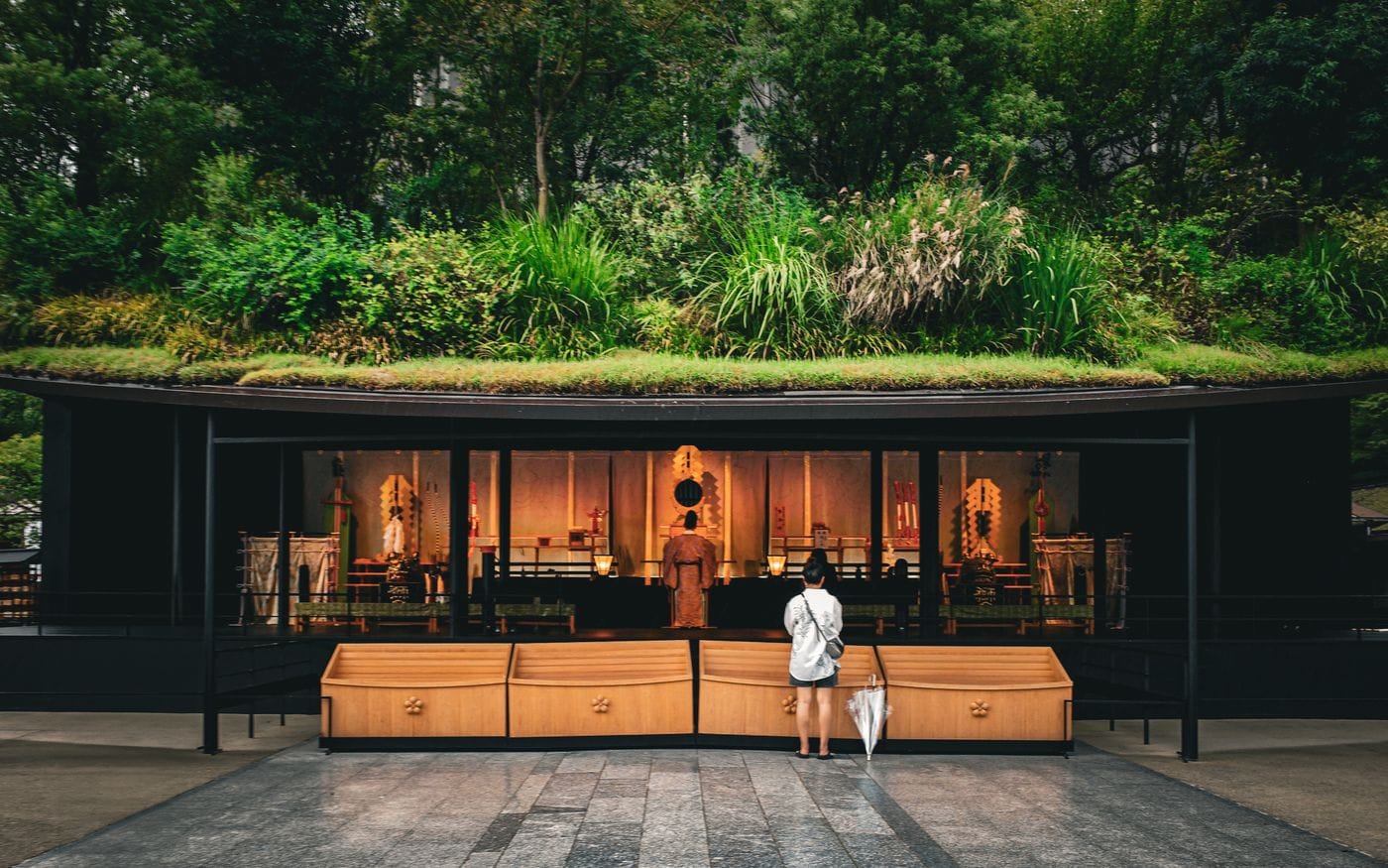 A visitor stands before a shrine at Dazaifu, Fukuoka, surrounded by lush greenery and traditional architecture.