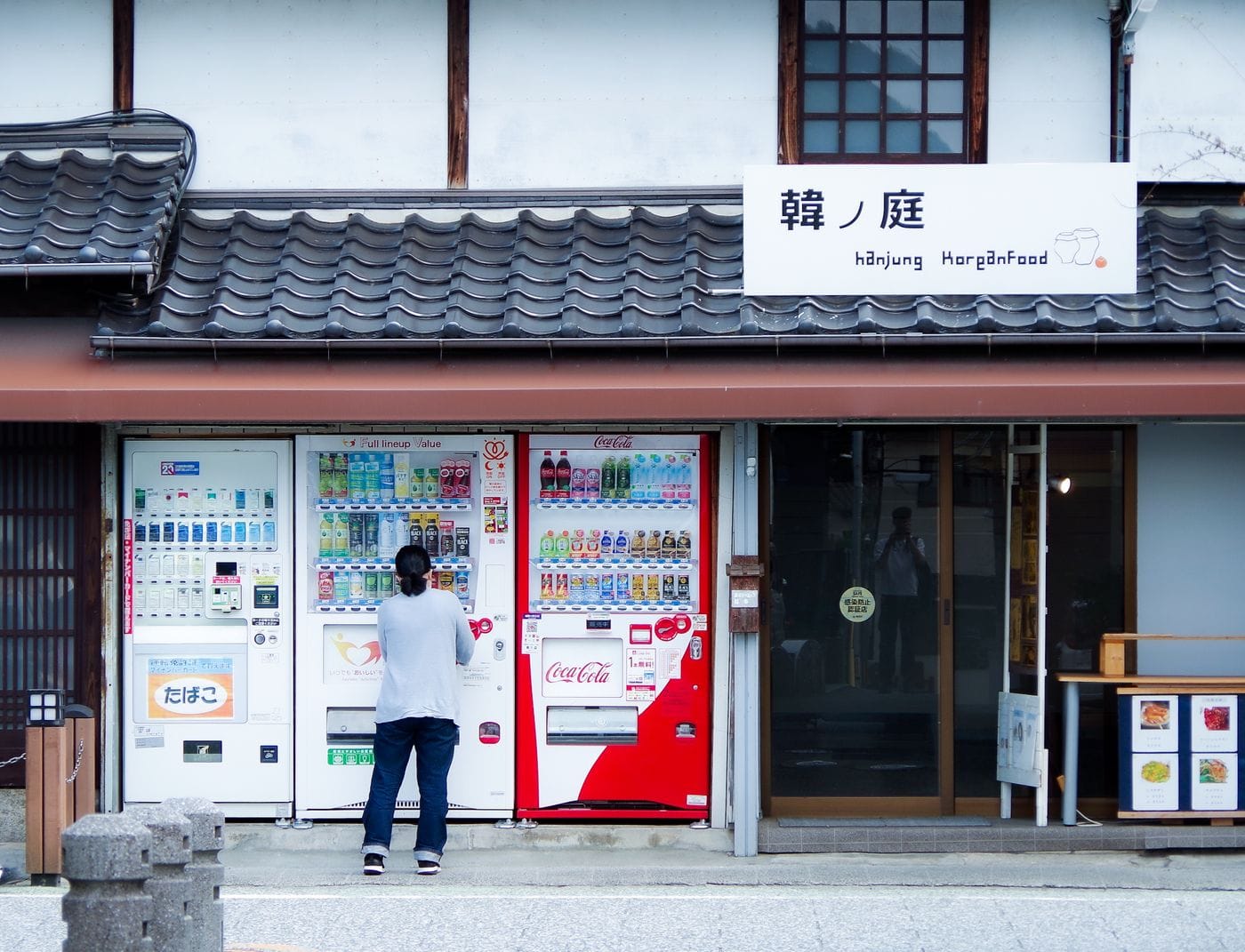 An individual standing at vending machines on a Japanese street under traditional architecture.
