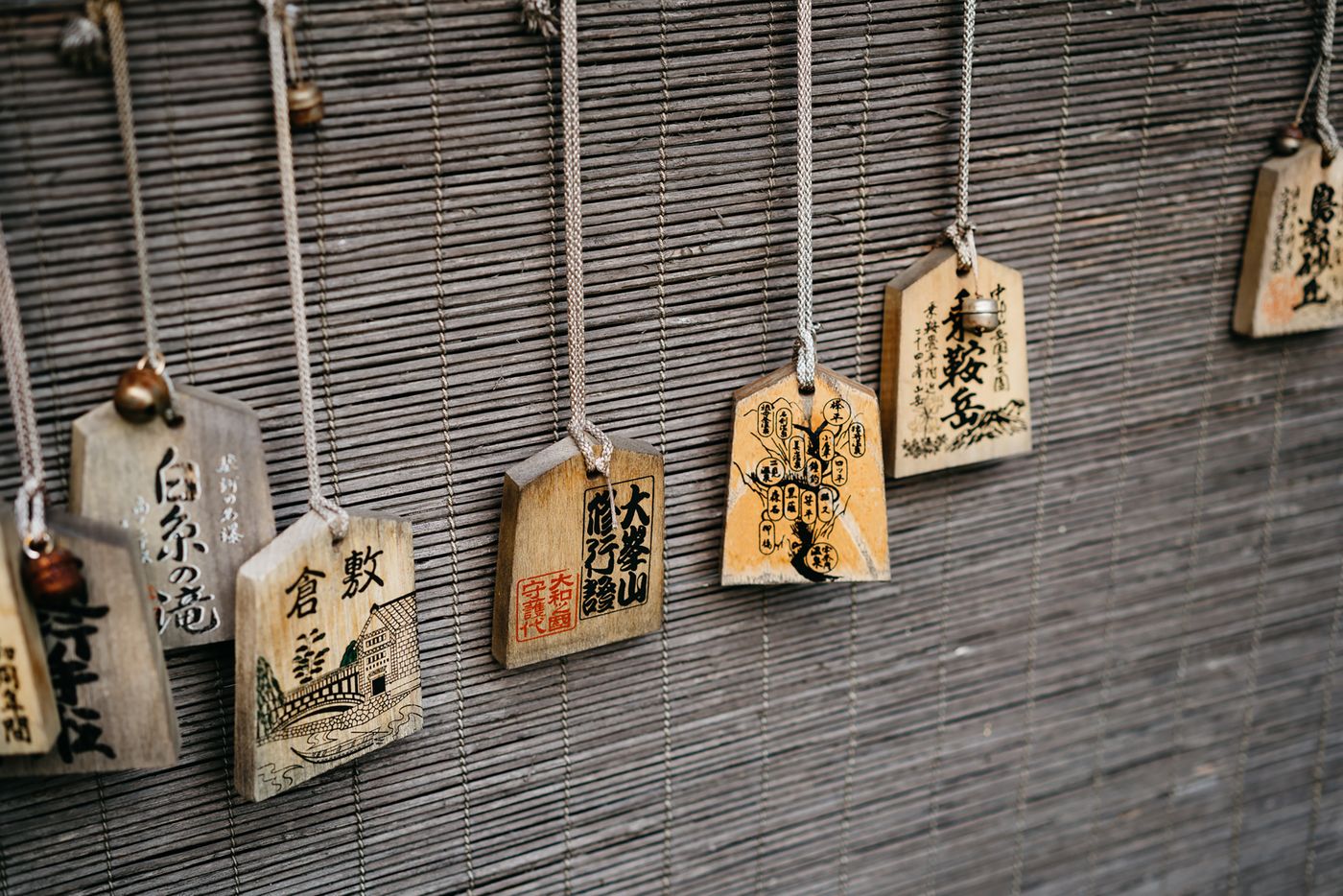 Close-up of traditional Japanese ema wooden plaques hanging on a bamboo mat in a shrine setting.