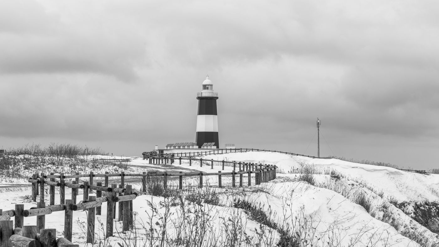 Black and white photo of a lighthouse amid snowy dunes in Abashiri, Hokkaido, Japan.