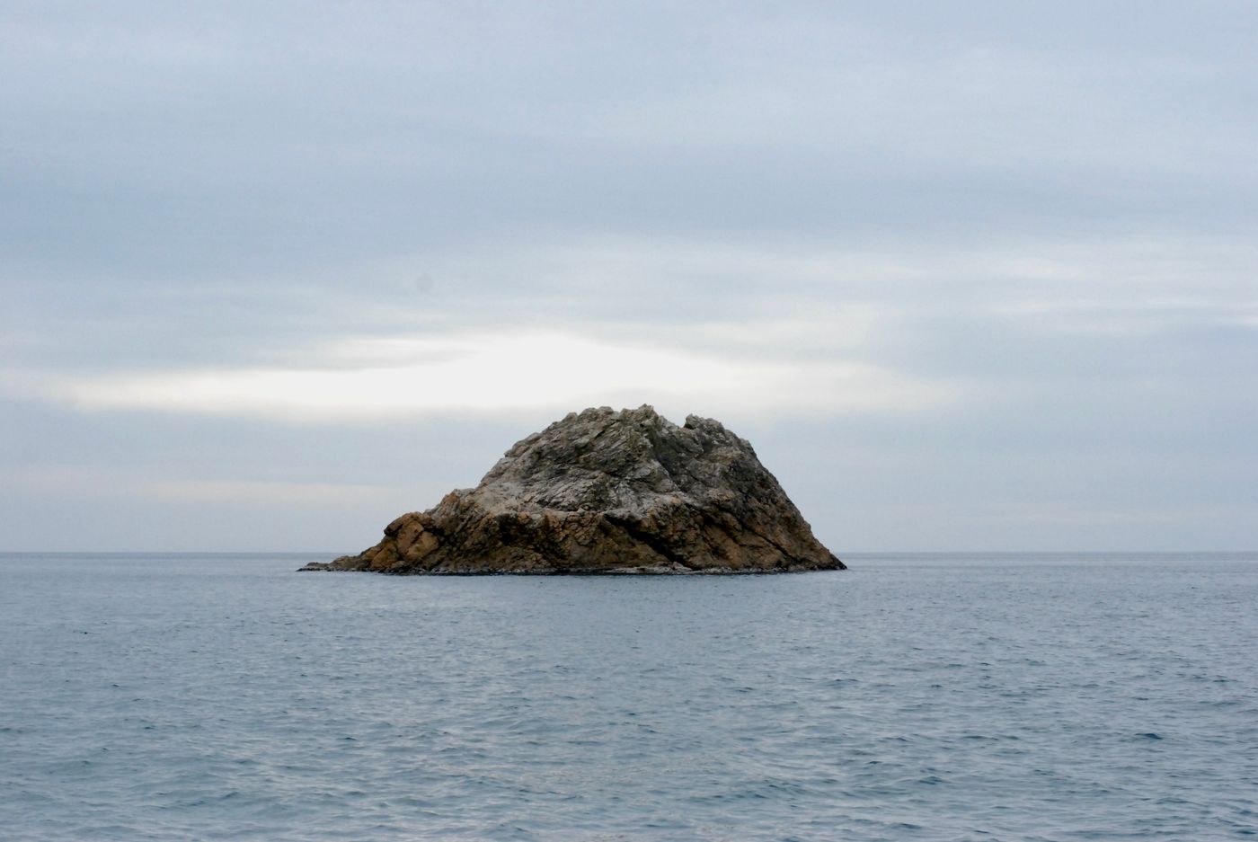 Peaceful rocky island surrounded by calm sea waters under a cloudy sky in Murakami, Niigata, Japan.