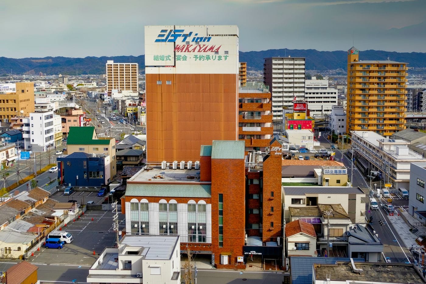 Aerial view of urban Wakayama cityscape with colorful buildings and distant hills.