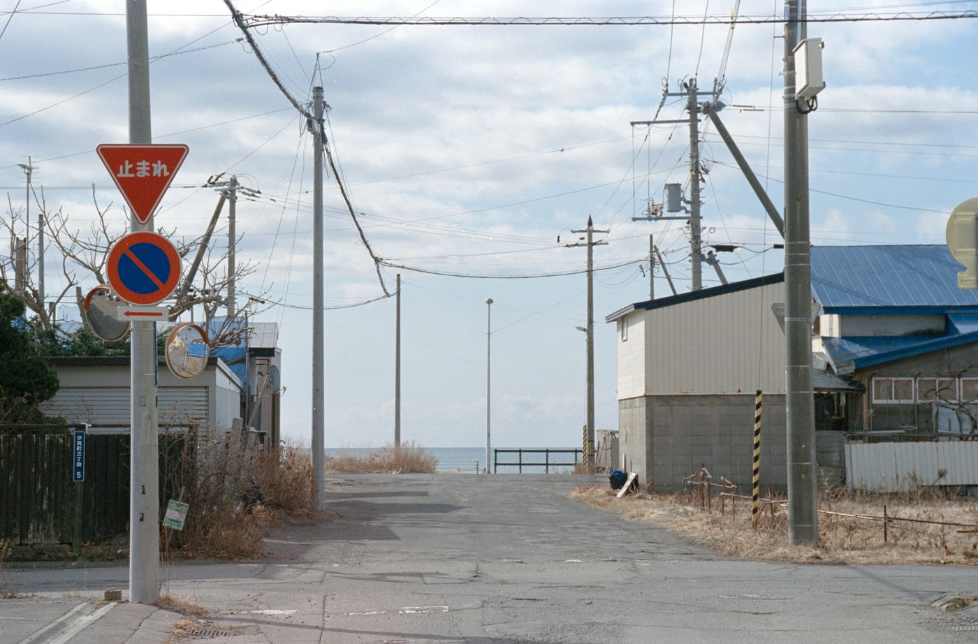 Deserted street scene leading to ocean filled with utility poles and signs nearby.