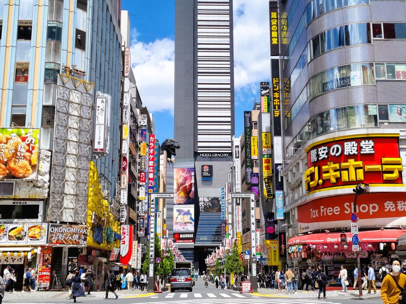 Bustling street in Shinjuku, Tokyo with vibrant advertisements and iconic Godzilla statue.