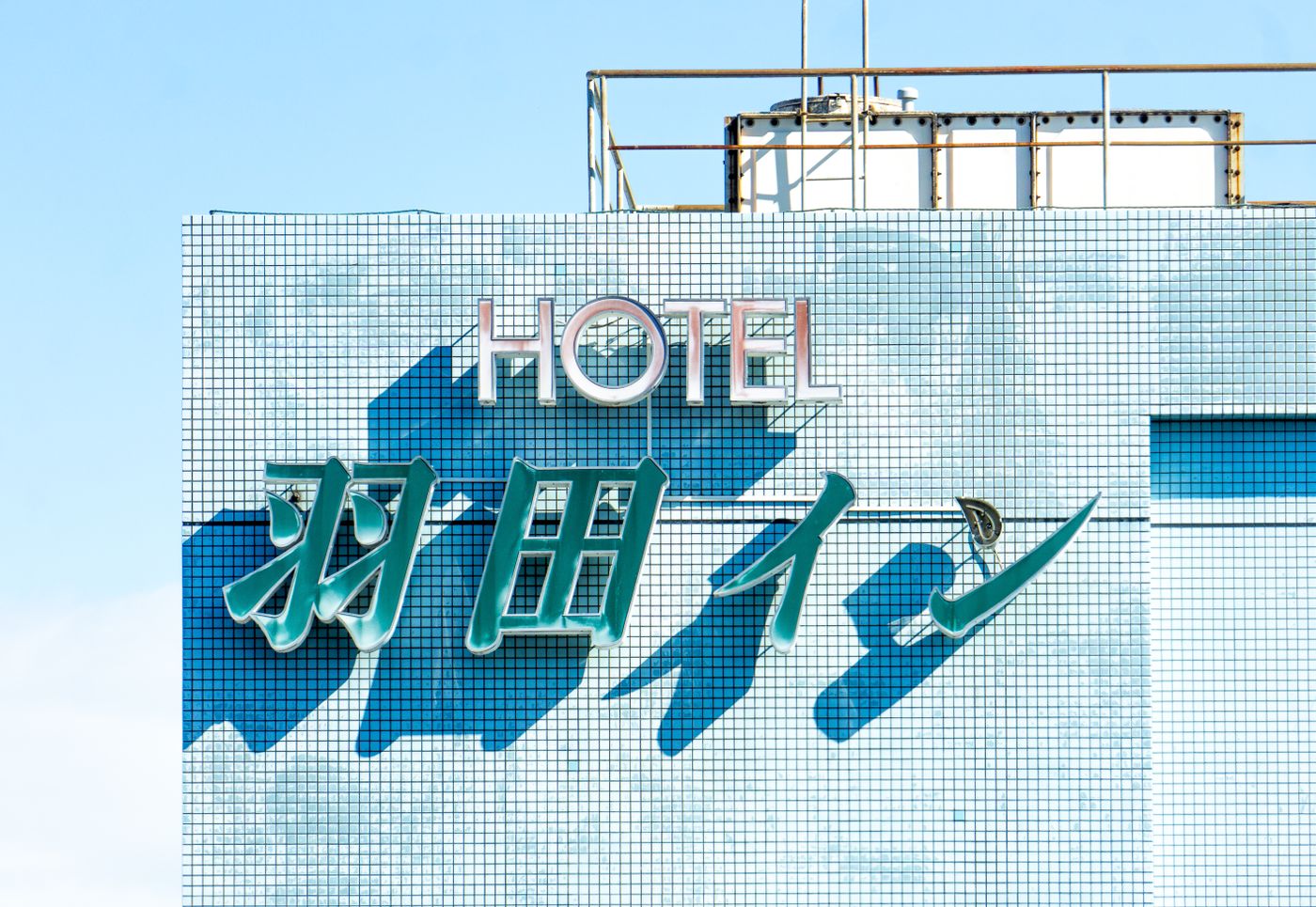 Brightly lit hotel sign with blue tiles under a clear sky, showcasing modern architecture.