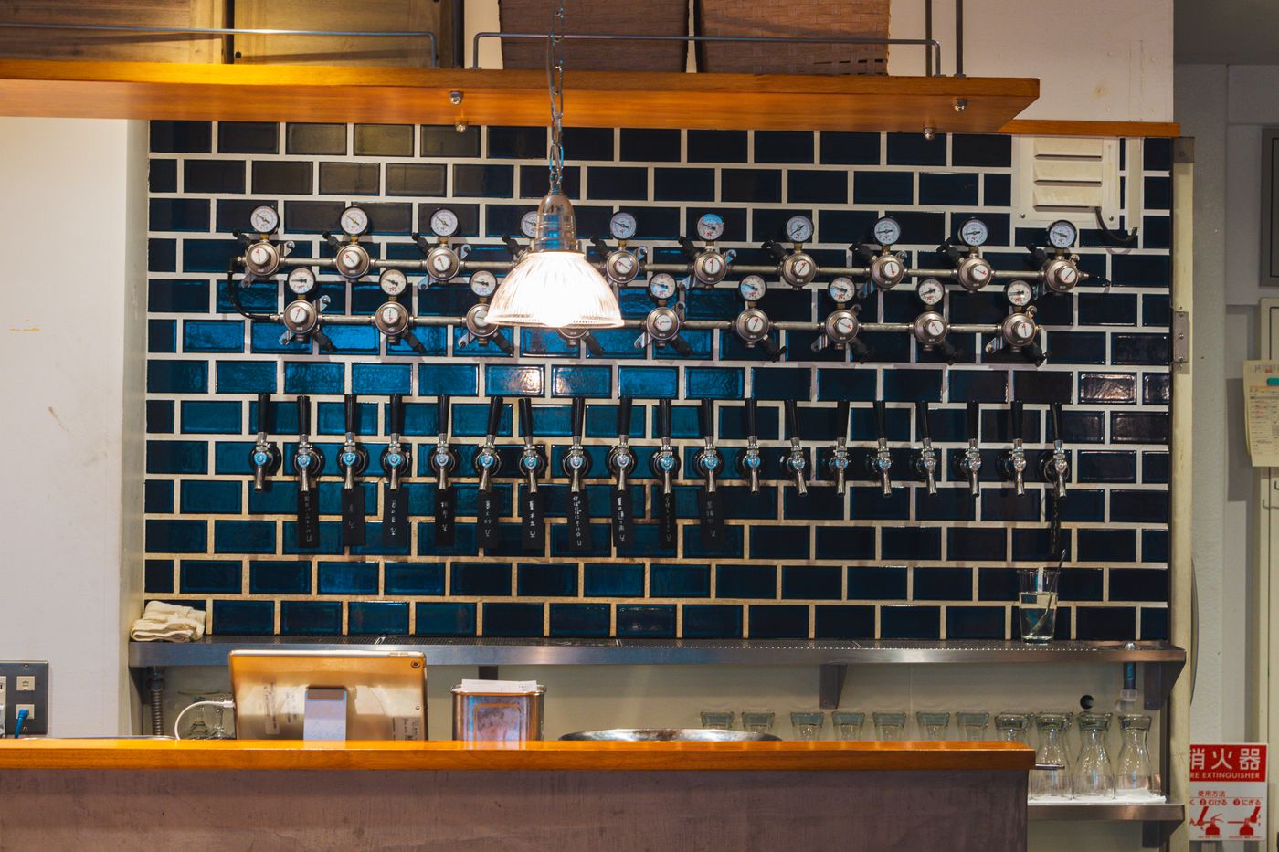 Modern craft beer bar interior in Adachi City, Tokyo, featuring multiple beer taps on a brick wall.