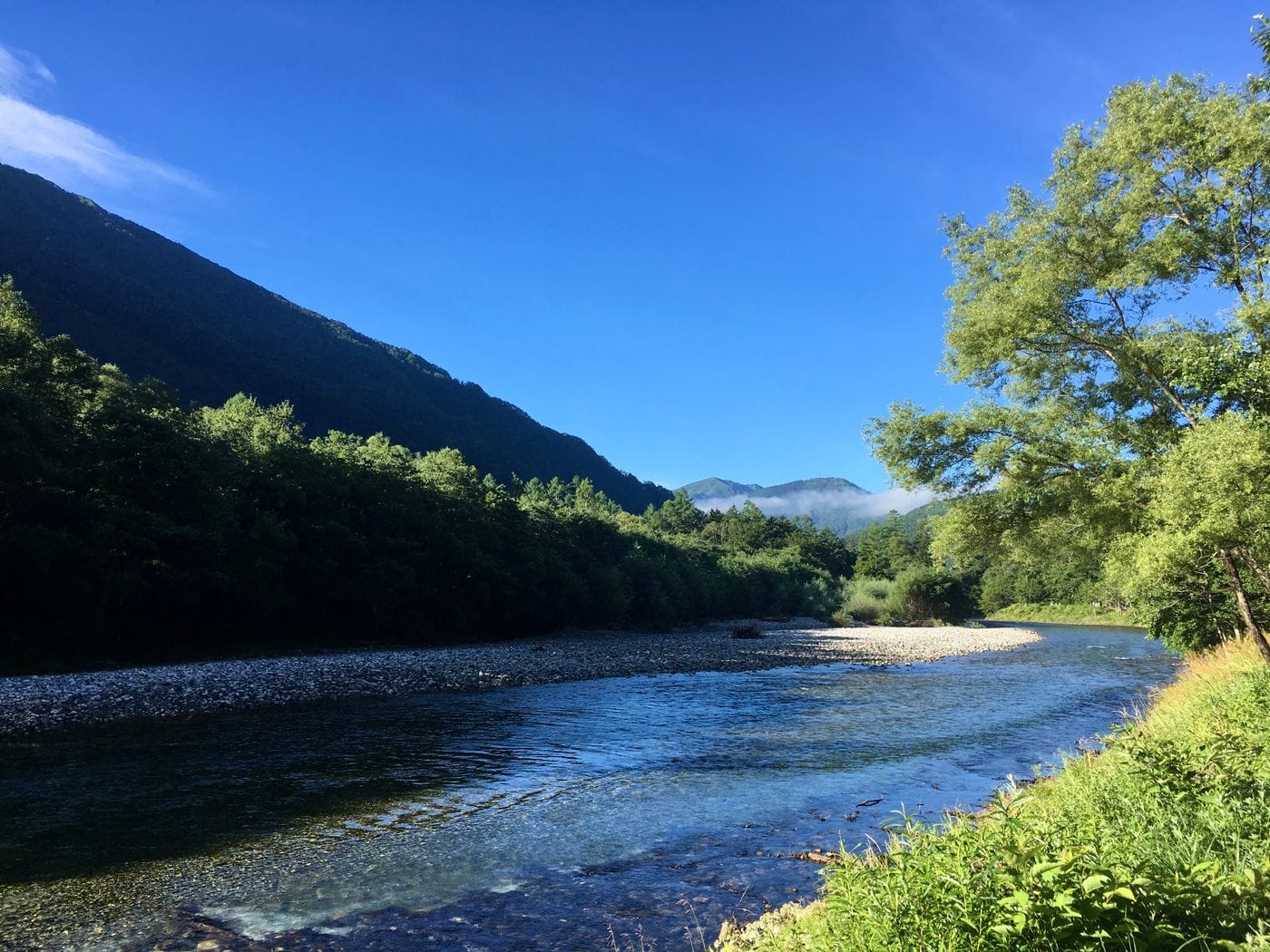 Serene view of a tranquil river and lush greenery in Kamikochi, a picturesque part of the Japanese Alps.