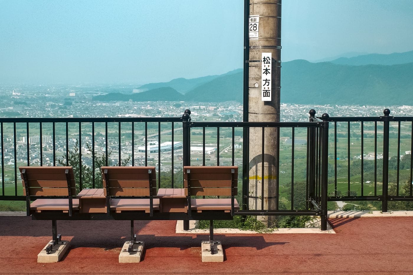Tranquil hilltop view overlooking Nagano, Japan with empty benches and mountain backdrop.