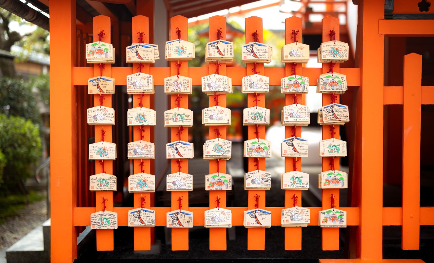 Vibrant ema plaques on an orange shrine wall in Kyoto, Japan, symbolizing prayers and wishes.