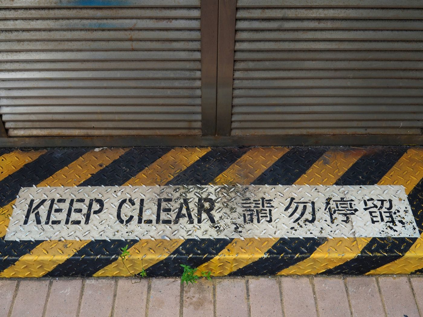 A bilingual 'Keep Clear' safety sign on a rusty metal floor in Hong Kong.