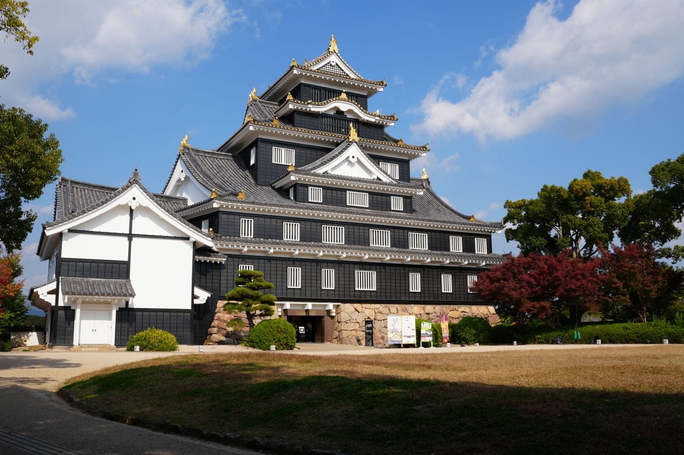 Okayama Castle with traditional architecture and colorful autumn foliage under clear sky.