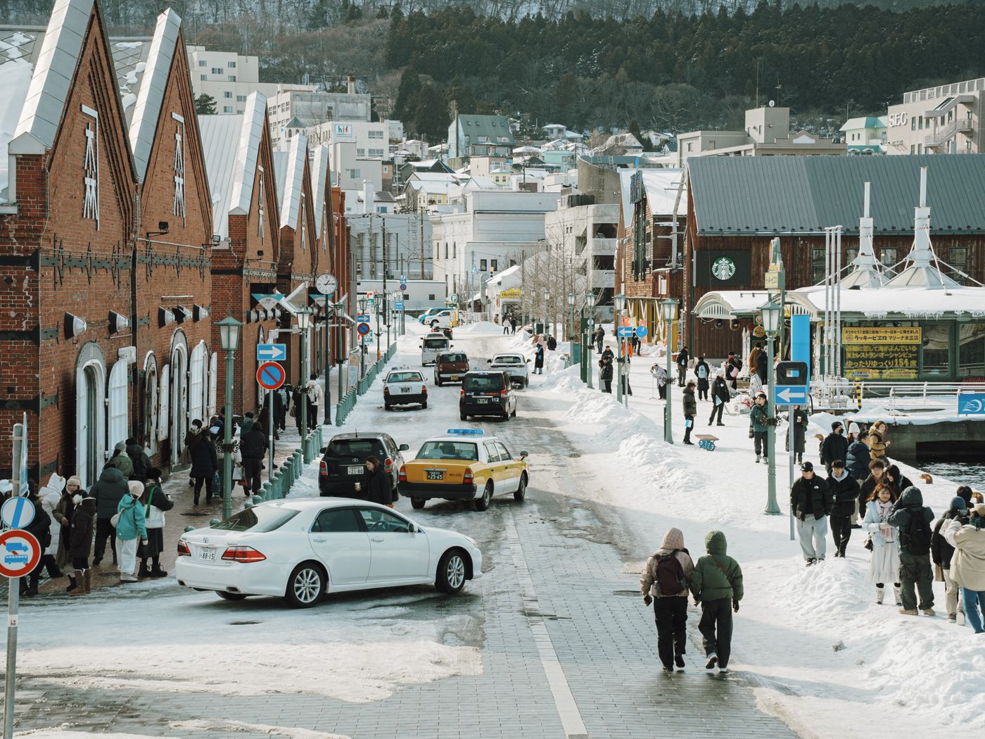 A vibrant winter street scene in Hakodate, Japan, with people and cars on a snowy day.