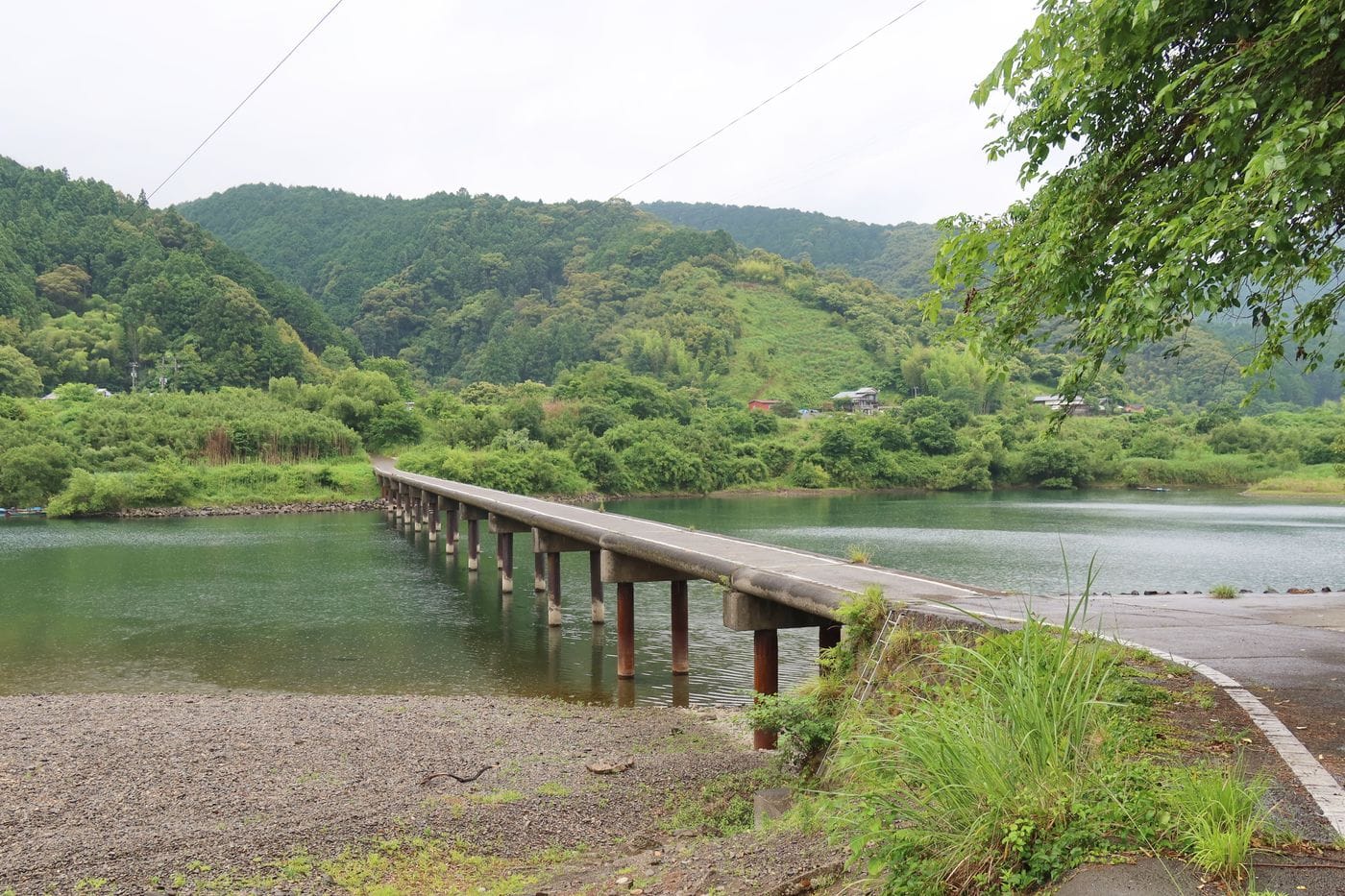 A serene scene of a long bridge over a calm river in Kochi Prefecture, Japan surrounded by lush greenery.