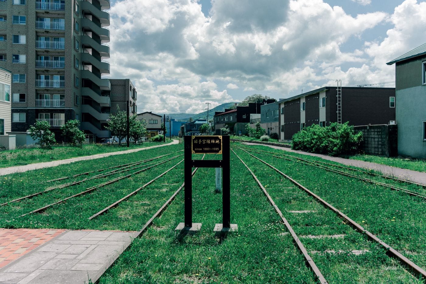 An old railway track amidst urban buildings in Hokkaido, Japan under a cloudy sky.