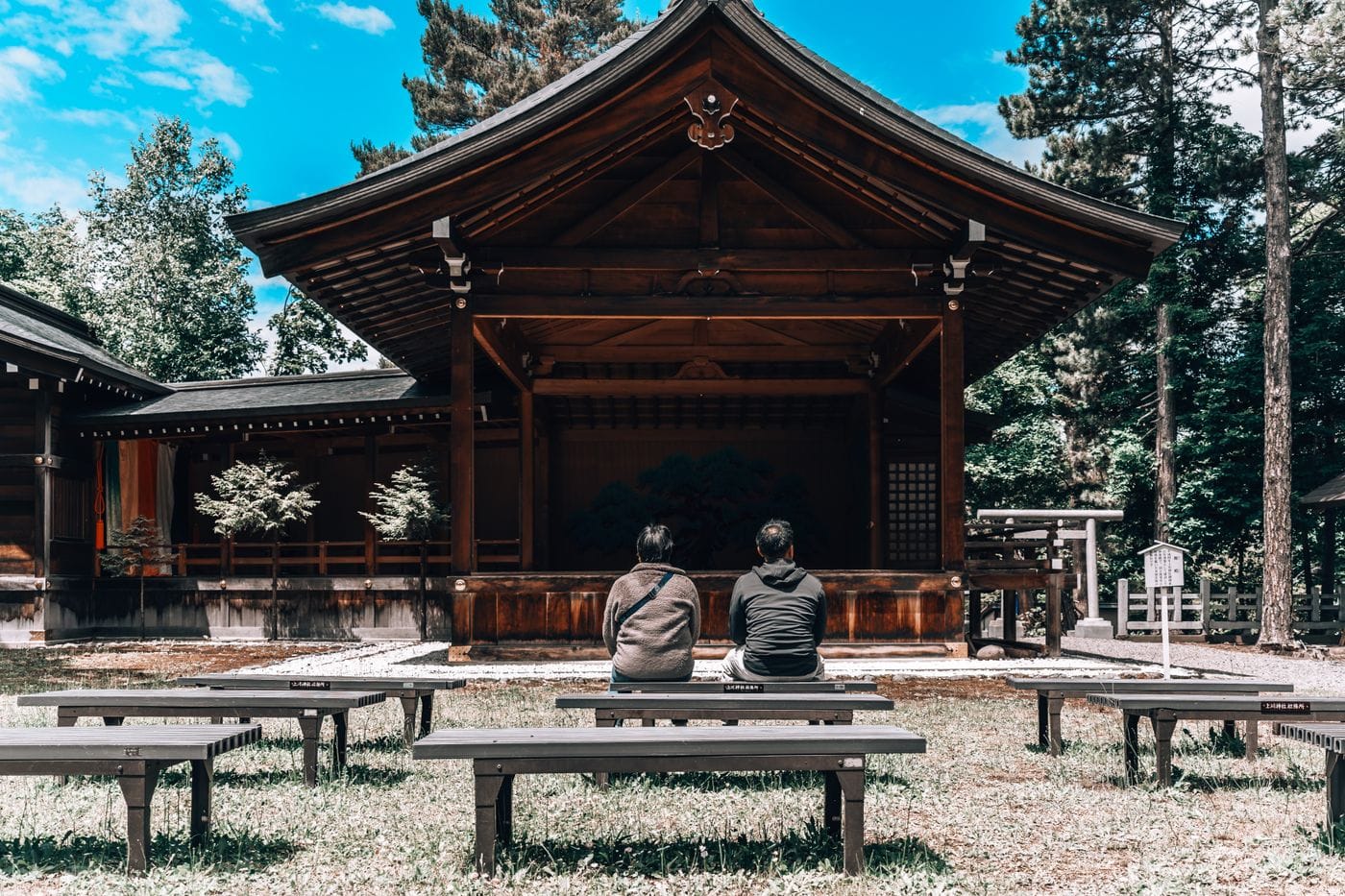 Two people sitting in front of a traditional wooden shrine in a serene Hokkaido setting.