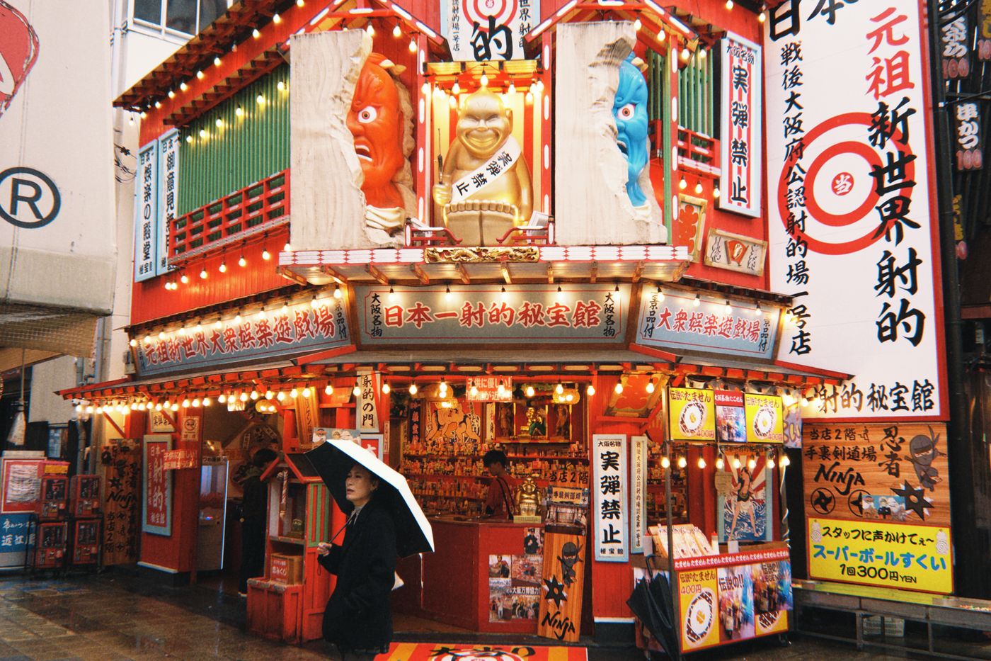Colorful street scene of Dotonbori, Osaka with a woman under an umbrella during a rainy day.