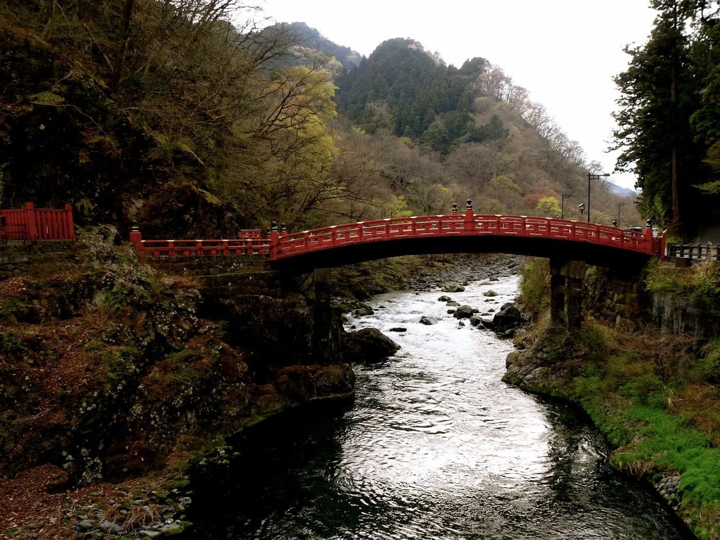 Picturesque view of red Shinkyo Bridge over a river surrounded by lush forest in Nikko, Japan.