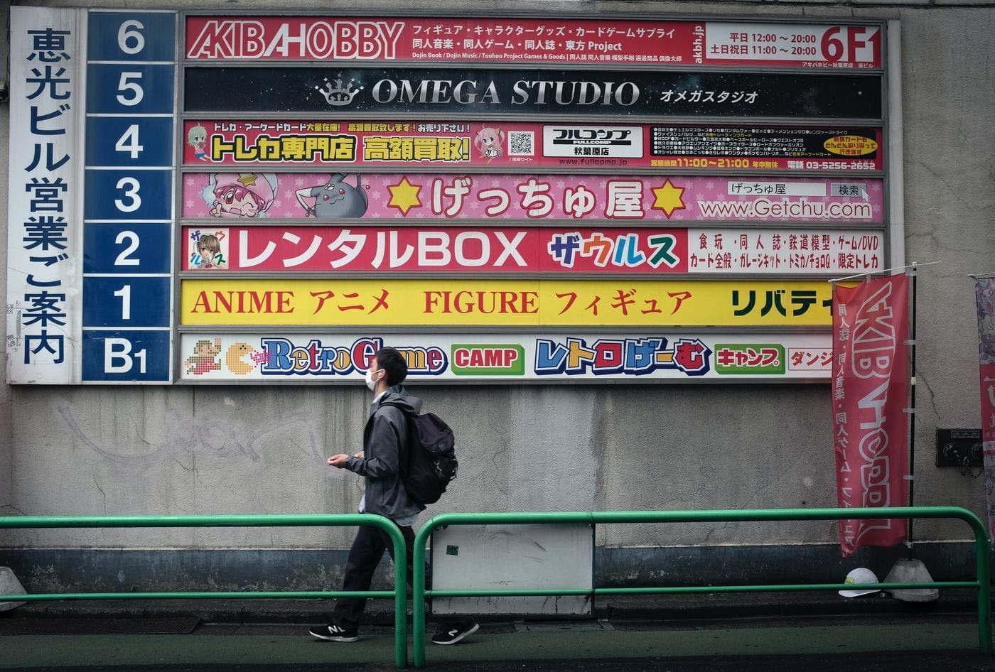Man walking past colorful anime and hobby store signs in Taito City, Tokyo, Japan.