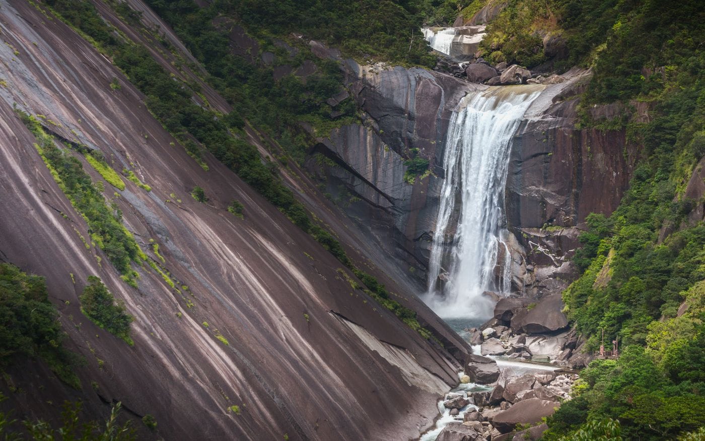 Stunning waterfall cascading down rocky cliffs in Yakushima, Japan, surrounded by lush greenery.